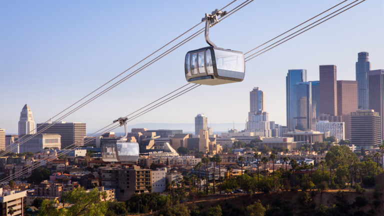 A cable car travels above a cityscape with tall buildings in the background, possibly related to Los Angeles public transit.